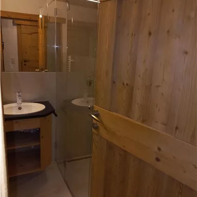 Ein modernes Badezimmer mit einer Dusche aus Glas und einem Waschbecken aus Holz. Die Wände sind hell und der Boden ist dekoriert.