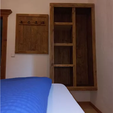 Ein gemütliches Zimmer mit einem Bett und einem Holzregal an der Wand. Neben dem Regal befindet sich eine Hakenleiste aus Holz.