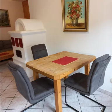 Ein gemütlicher Essbereich mit einem Holztisch und zwei grauen Stühlen. An der Wand hängt ein Blumenbild, und im Hintergrund steht ein Kamin.