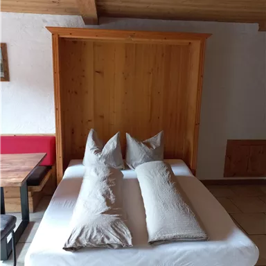 Ein gemütliches Schlafzimmer mit einem Klappbett aus Holz und zwei Kissen. Die Einrichtung ist schlicht und einladend.
