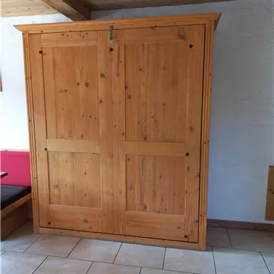 Ein großer Holzschrank mit doppeltürigem Design steht in einem Raum. Der Boden ist mit schönen Fliesen ausgelegt.