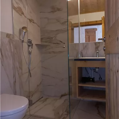 Ein modernes Badezimmer mit einer transparenten Dusche und eleganten Marmorelementen. Es gibt eine Toilette und einen Holzunterbau mit Stauraum.