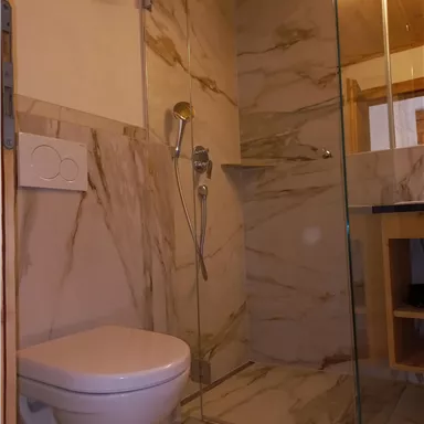 Ein modernes Badezimmer mit einer gläsernen Duschkabine und eleganten Marmorfliesen. Eine Toilette ist ebenfalls vorhanden, die den Raum ergänzt.