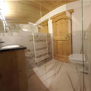 Ein modernes Badezimmer mit Marmorböden und einer Glasdusche. Die Wände sind hell und es gibt eine Holzdecke sowie eine Holzschiebetür.