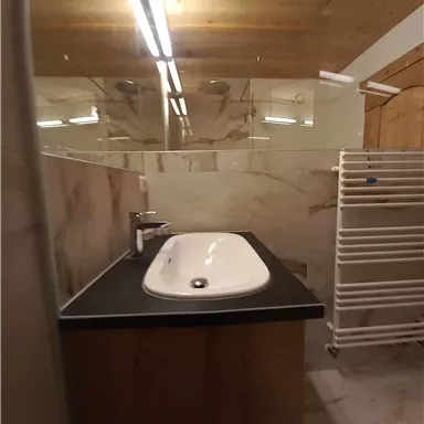 Ein modernes Badezimmer mit einem eleganten Waschbecken und einem Holz-Möbel. Die Wände sind mit hellem Marmor gefliest und es gibt ein Handtuchheizkörper.