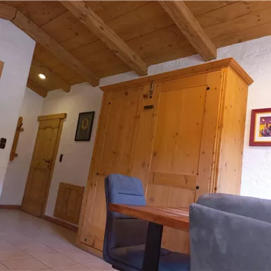 Ein gemütlicher Wohnraum mit Holzvertäfelung und einem großen Kleiderschrank. Der Raum enthält einen Tisch und Stühle sowie eine Tür, die zu einem weiteren Bereich führt.