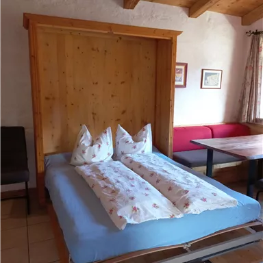 Ein gemütliches Zimmer mit einem klappbaren Bett und zwei Kissen. An der Wand ist Holzvertäfelung, und es gibt einen Esstisch mit Stühlen.