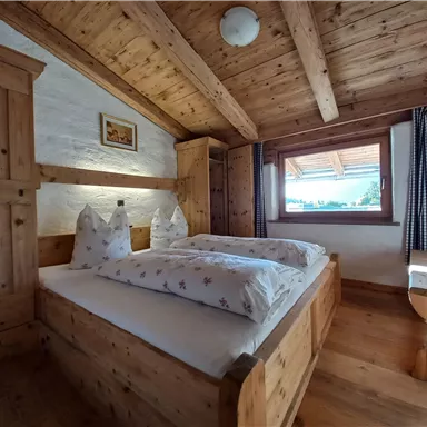 Ein gemütliches Zimmer mit Holzdecken und -möbeln. Zwei Betten mit weißen Kissen und Ausblick auf die Natur.