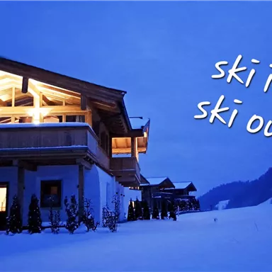 A modern chalet in a snowy landscape at twilight. The inscription "ski in ski out" indicates proximity to the slopes.