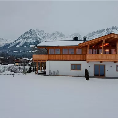 A modern house in the winter landscape with lots of snow. Majestic mountains are visible in the background.