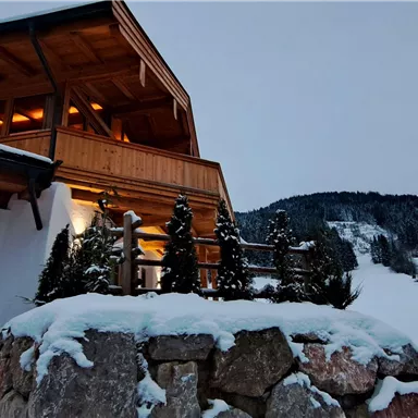 A modern wooden house in a snow-covered landscape. In the background, gentle hills and a clear evening sky can be seen.