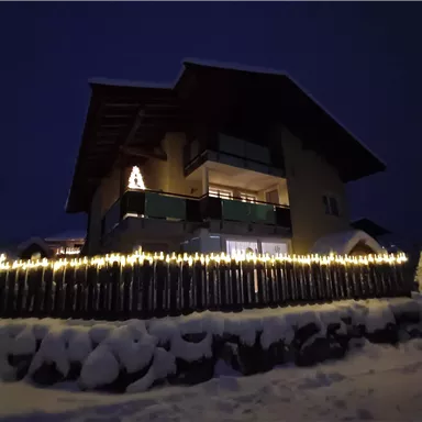 Ein gemütliches Haus im Schnee, beleuchtet von Lichtern. Die dunkle Nacht schafft eine festliche Atmosphäre.