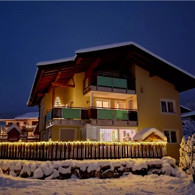 Ein gemütliches Haus im Schnee, beleuchtet von Lichtern. Die Umgebung ist winterlich und friedlich.