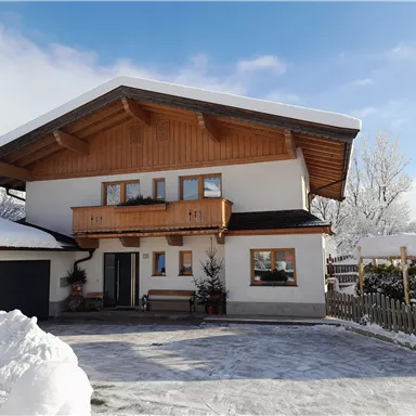 A cozy house in the snow with a snow-covered garden. The blue sky and sunny conditions create an inviting atmosphere.