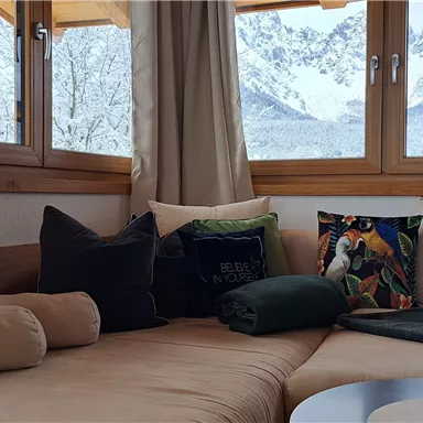 A cozy living room with a comfortable seating area and large windows. Outside, snow-covered mountains are visible.