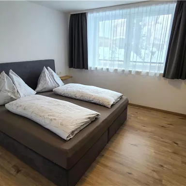 Ein modernes Schlafzimmer mit einem Doppelbett und zwei Kissen. Große Fenster lassen viel natürliches Licht herein.