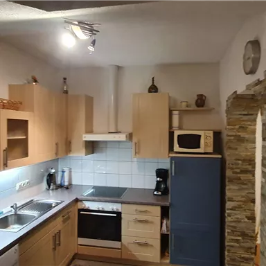 A modern kitchen with light wooden furniture and a tiled floor. The room is well-lit and feels inviting.