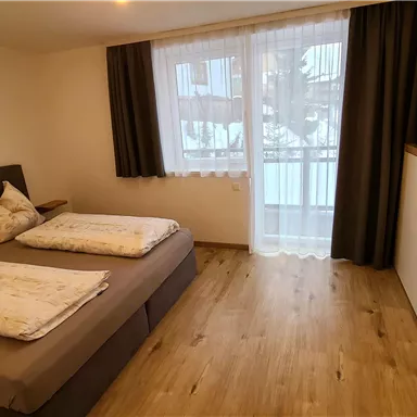 Ein gemütliches Schlafzimmer mit zwei Betten und moderner Einrichtung. Große Fenster sorgen für viel Tageslicht und eine angenehme Atmosphäre.