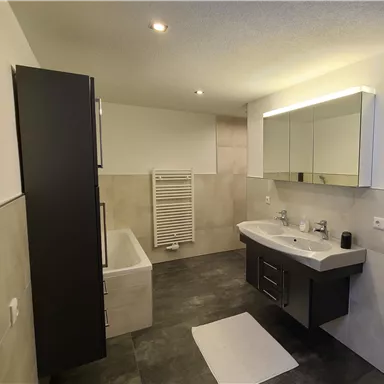 Ein modernes Badezimmer mit einer Badewanne, einer großen Waschtischzeile und einem Handtuchheizkörper. Die Wände sind in neutralen Tönen gehalten und die Beleuchtung ist hell und einladend.