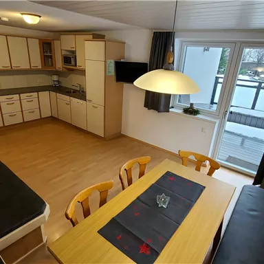 Eine moderne Küche mit einem großen Esstisch und gemütlichen Stühlen. Große Fenster sorgen für viel Tageslicht.