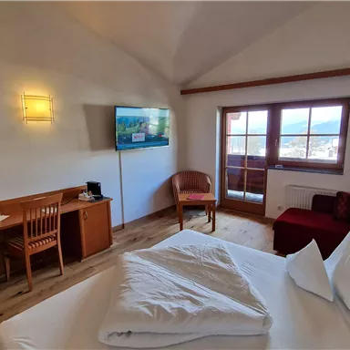 A cozy room with a double bed, a television, and a balcony. There is a table and chairs as well as a modern, bright style.