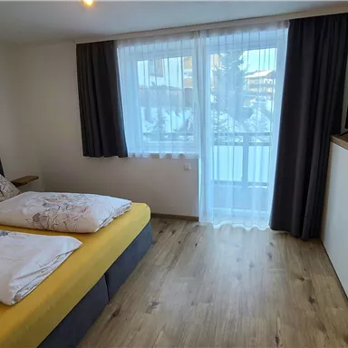 Ein modernes Schlafzimmer mit zwei Betten, einem Fernseher und einem Balkon. Große Fenster sorgen für viel Tageslicht.