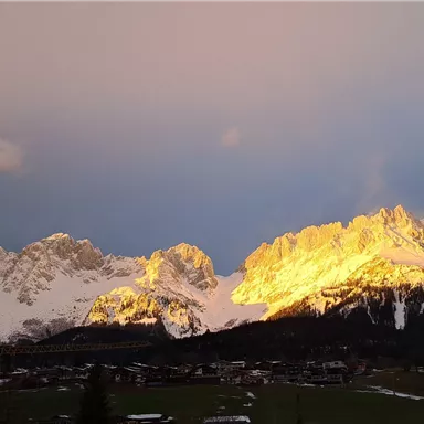A majestic mountain landscape with snow-covered peaks that shine in the sunlight. The sky is lightly clouded, giving the scene a special atmosphere.
