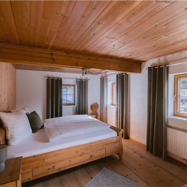 Ein gemütliches Schlafzimmer mit Holzwänden und einem Doppelbett. Es gibt zwei Fenster mit Vorhängen und einen sanften Teppich auf dem Boden.