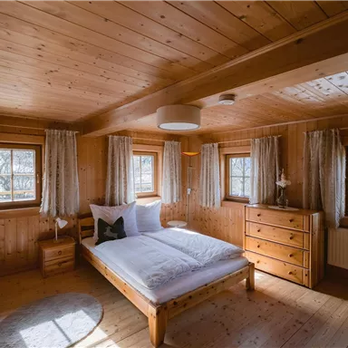 Ein gemütliches Schlafzimmer mit Holzverkleidung und großen Fenstern. Das Bett ist schlicht und einladend, ideal für einen ruhigen Aufenthalt.