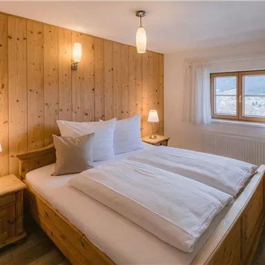 Ein gemütliches Schlafzimmer mit Holzwänden und zwei Betten. Es gibt Nachttische mit Lampen und ein Fenster, das viel Licht reinlässt.