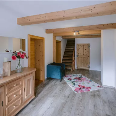 Ein heller Eingangsbereich mit Holzdetails und einer Treppe im Hintergrund. Eine Blumenvase und ein Teppich verleihen dem Raum eine einladende Atmosphäre.