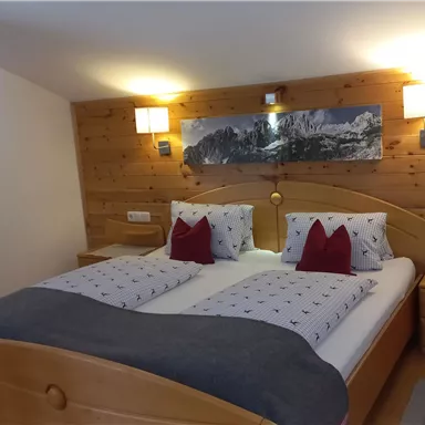 Ein gemütliches Schlafzimmer mit Holzwänden und einem Doppelbett. Die Kissen sind dekorativ, und es gibt Nachttische sowie sanfte Beleuchtung.