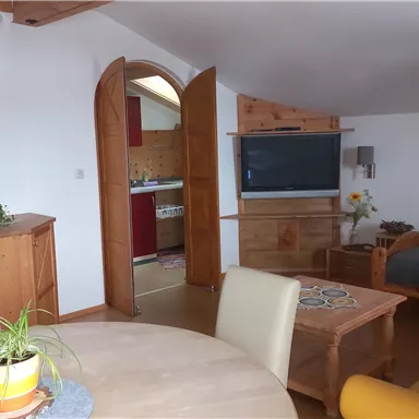 Eine gemütliche Wohnungecke mit einem Tisch, Stühlen und einem Sofa. Die Einrichtung ist hell und modern, mit einer offenen Küche im Hintergrund.