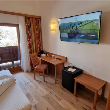 A cozy hotel room with a bed, a television, and a small desk. Bright colors and a pleasant atmosphere create an inviting environment.