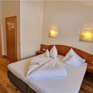 A cozy hotel room with a large bed and two pillows. In the background, a modern bathroom is visible.