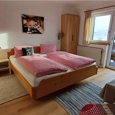 Ein gemütliches Schlafzimmer mit einem großen Doppelbett und Holzschränken. Durch das Fenster ist ein schöner Ausblick zu sehen.