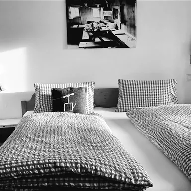 Ein stilvolles Schlafzimmer mit einem großen Bett und karierten Bettdecken. An der Wand hängt ein Schwarz-Weiß-Bild.