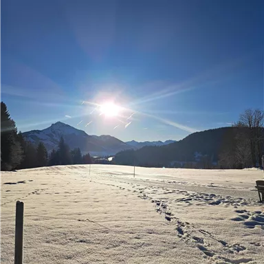 Eine schneebedeckte Landschaft unter einem klaren blauen Himmel. Die Sonne strahlt hell über den Bergen.