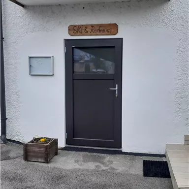 An entrance door to a ski and storage room. The wall is white, and above the door hangs a wooden sign with the inscription "SKI & Storage Room".