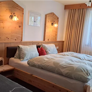A cozy bedroom with two wooden beds. There is soft lighting, bright curtains, and a window that lets in daylight.