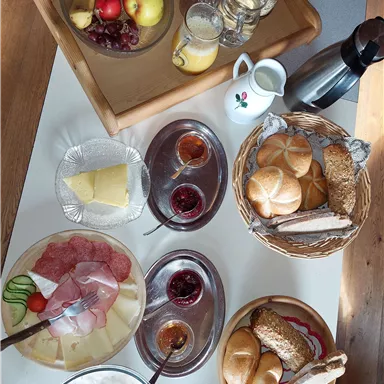A hearty breakfast with fresh fruit, bread, cheese, and cold cuts. There are also jams and various drinks.