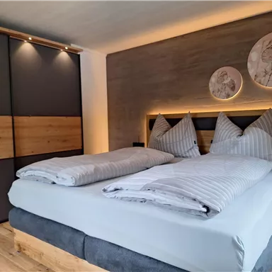 A modern bedroom with a double bed and elegant wood paneling. Soft lighting and decorative wall art create a cozy atmosphere.