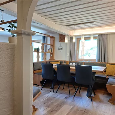 A cozy dining area with a large table and several chairs. The decor is modern with wooden paneling and large windows that let in plenty of light.