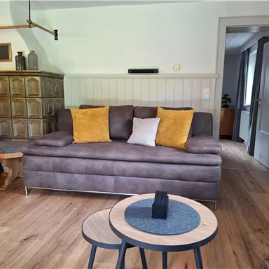 A cozy living room with a gray sofa and colorful cushions. The room has a modern wooden floor and a small table in the middle.