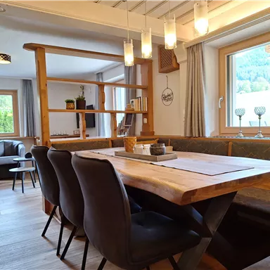 A cozy dining area with a large wooden table and upholstered chairs. Bright windows create a friendly atmosphere in the room.