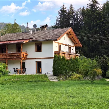 A beautiful house surrounded by green grass and trees. The wooden balcony gives the building a rustic charm.