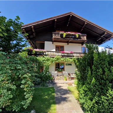 Ein schönes Alpenhaus mit einem großen Balkon und blühenden Pflanzen. Der Garten ist grün, gut gepflegt und lädt zum Verweilen ein.