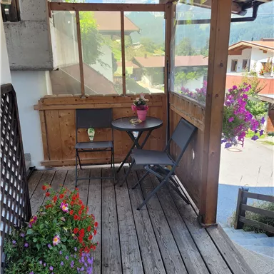 Ein gemütlicher Balkon mit einem kleinen Tisch und zwei Stühlen. Bunte Blumen in Blumentöpfen sorgen für eine einladende Atmosphäre.