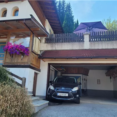 Ein großes Haus mit einem Balkon, der mit Blumen dekoriert ist. Vor dem Haus stehen ein Auto und ein Garagentor.