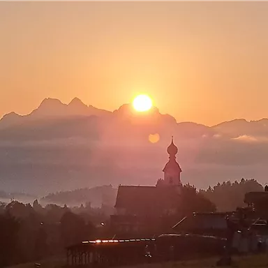 A stunning sunrise over the mountains. In the foreground, there is a church and gentle hills.